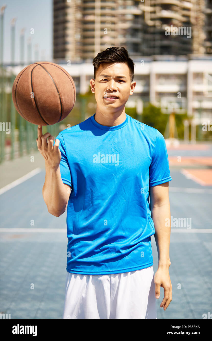 Jungen asiatischen Mann hält ein Basketball auf den Finger in die Kamera zu schauen. Stockfoto