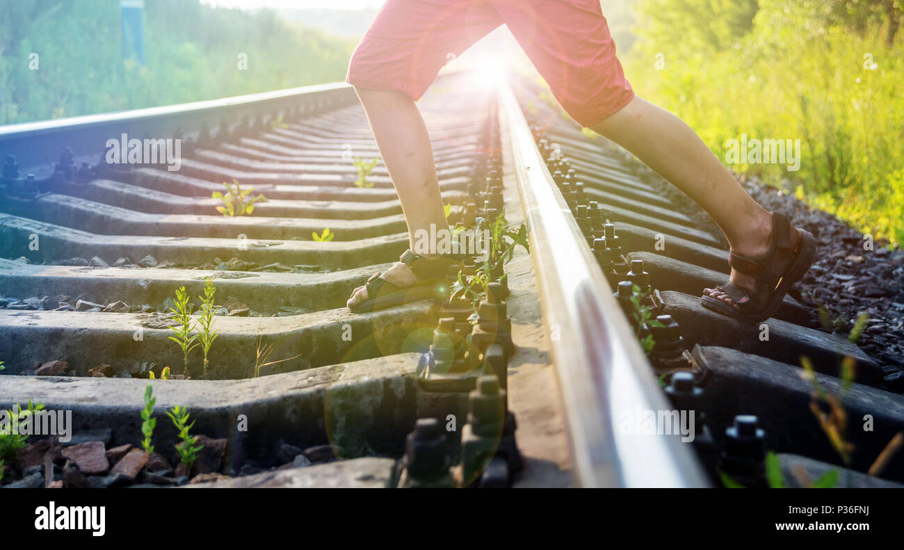 Jungen in roten Hosen mit dreckigen Füßen Schritte über die Schienen der Eisenbahn, die der Gefahr ausgesetzt Stockfoto