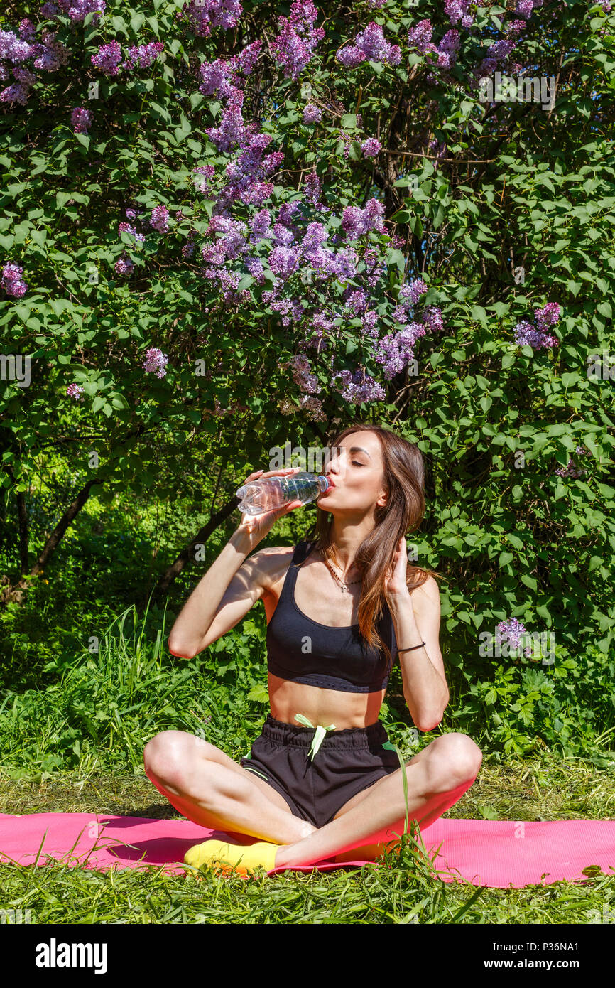 Junge, schöne Frau ist im Sport und Getränke sauberes Wasser in einem blühenden Garten eingerückt Stockfoto