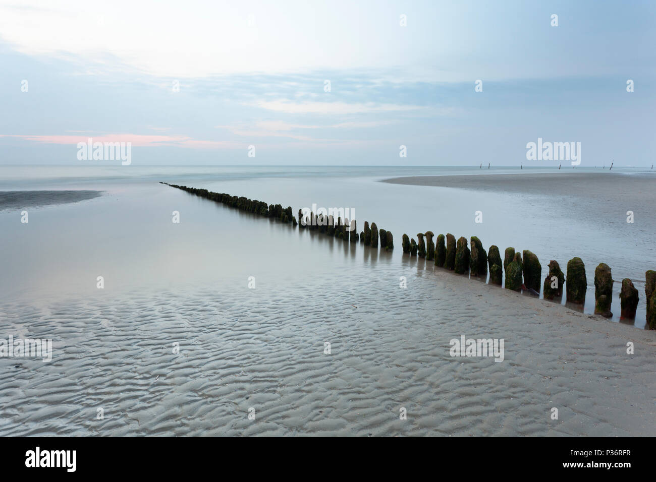 Eine Reihe von Stangen, die in der Nordsee in Norderney, Deutschland führt. Lange Belichtung geschossen. Stockfoto