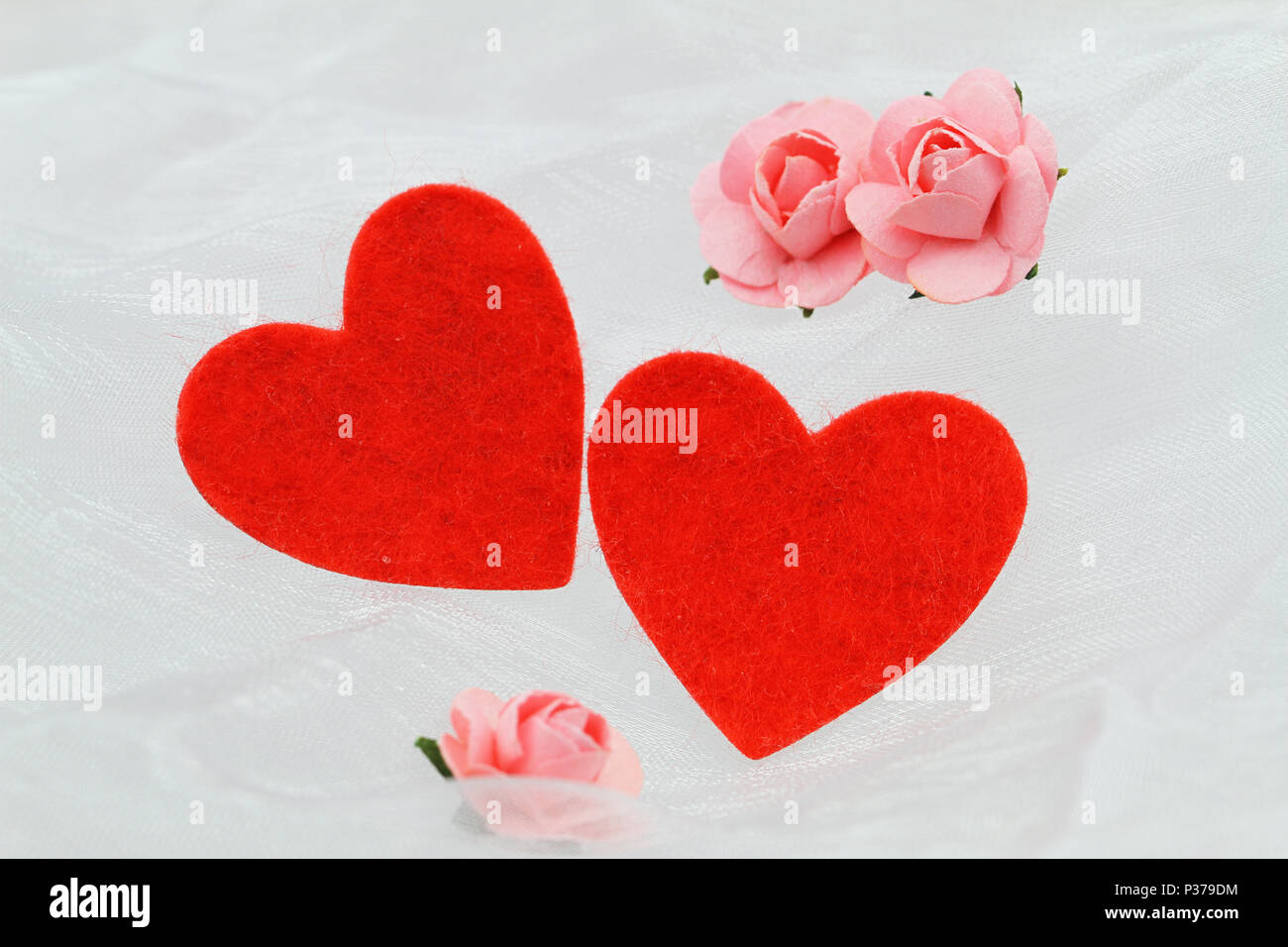 Zwei rote Herzen und kleine rosa Papier Rosen auf weißem Tuch mit Kopie Raum Stockfoto