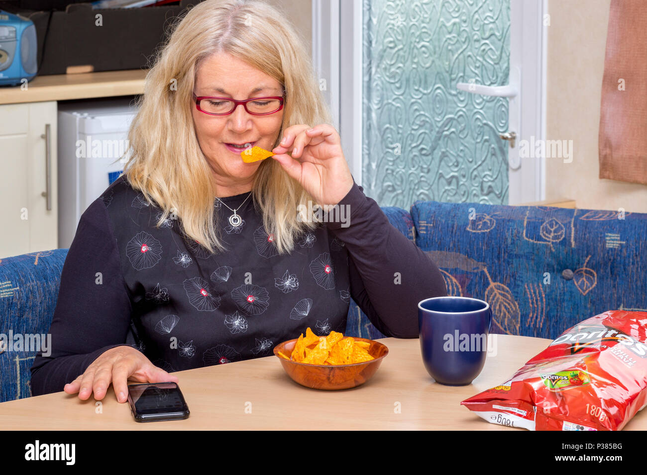 Blonde Frau isst Doritos aus ein Teilen Größe Tasche und eine kleine Schüssel Stockfoto