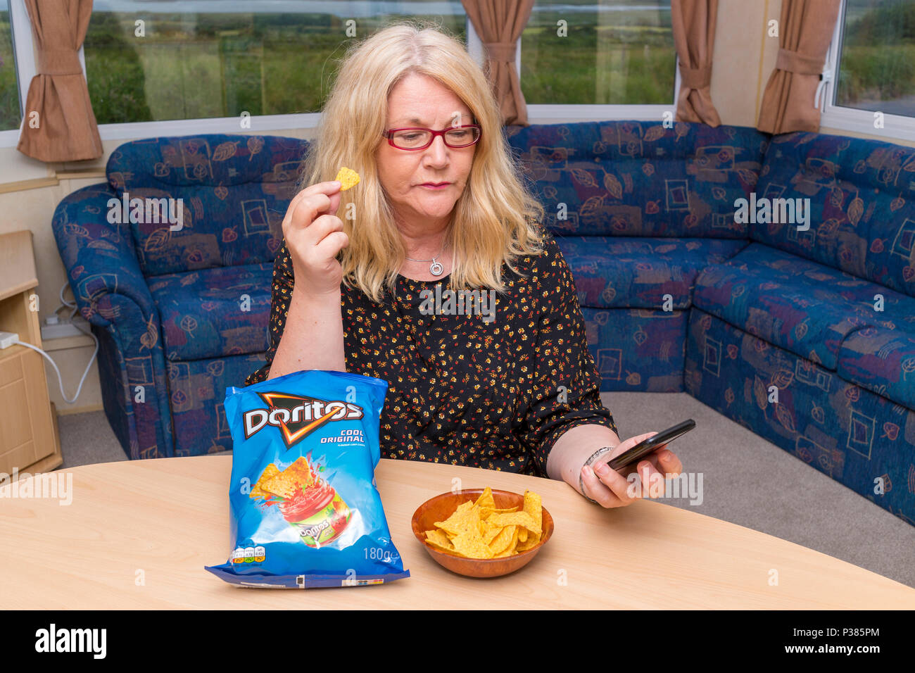 Blonde Frau isst Doritos aus ein Teilen Größe Tasche und eine kleine Schüssel Stockfoto