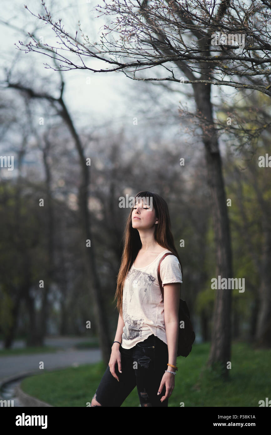 Attraktive junge Frau, die ihre Zeit geniessen draussen im Park. Kaukasische Mädchen mit langen braunen Haaren in ruhiger Pose und geschlossenen Augen. Stockfoto