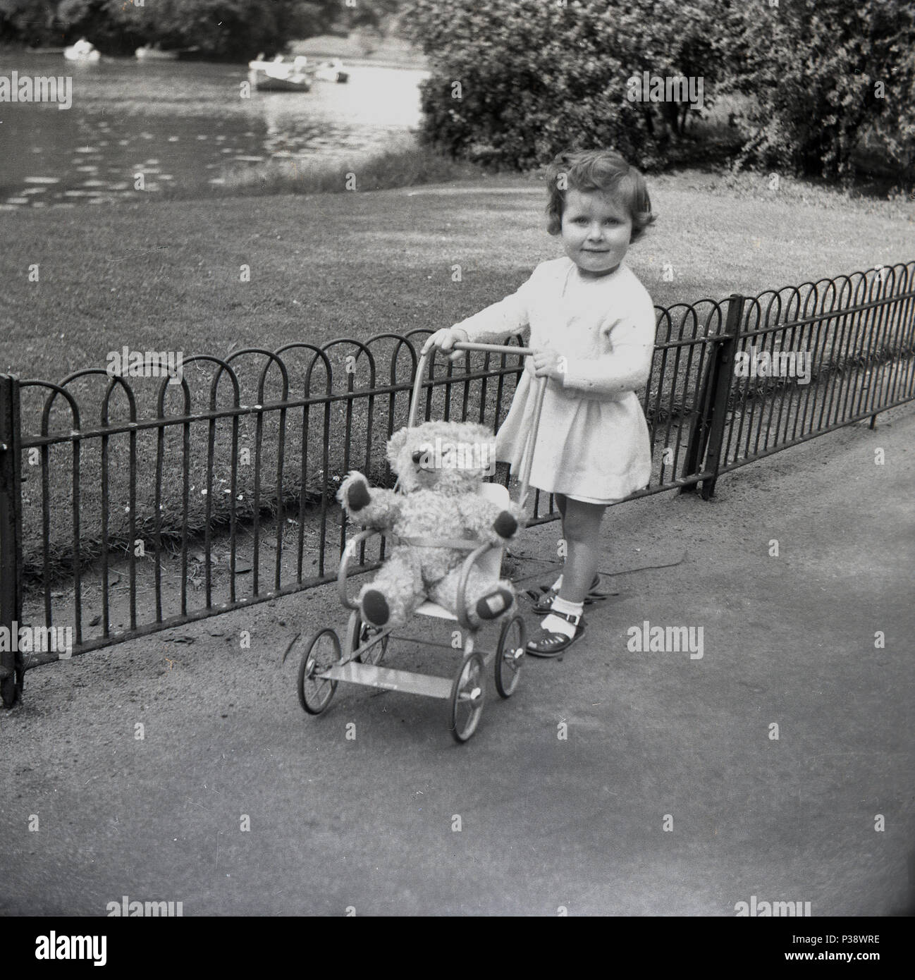1950, historische, junges Mädchen, im Freien in einem Park mit ihren Teddy Bär sitzend in ihr Spielzeug metall Kinderwagen, England, UK. Stockfoto