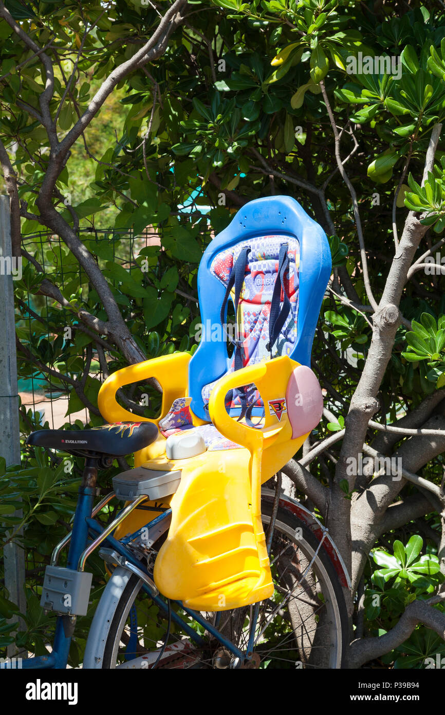 Das farbenfrohe Kunststoff Kindersitz Fahrrad für den Transport von einem Baby oder Kleinkind angebracht. Vor Sträuchern geparkt. Nähe zu sehen. Stockfoto