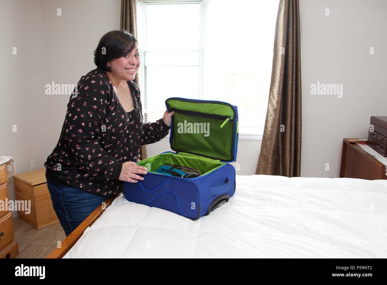 Eine Frau lächelt aufgeregt, als Sie Ihren gepackten Koffer schließt Stockfoto