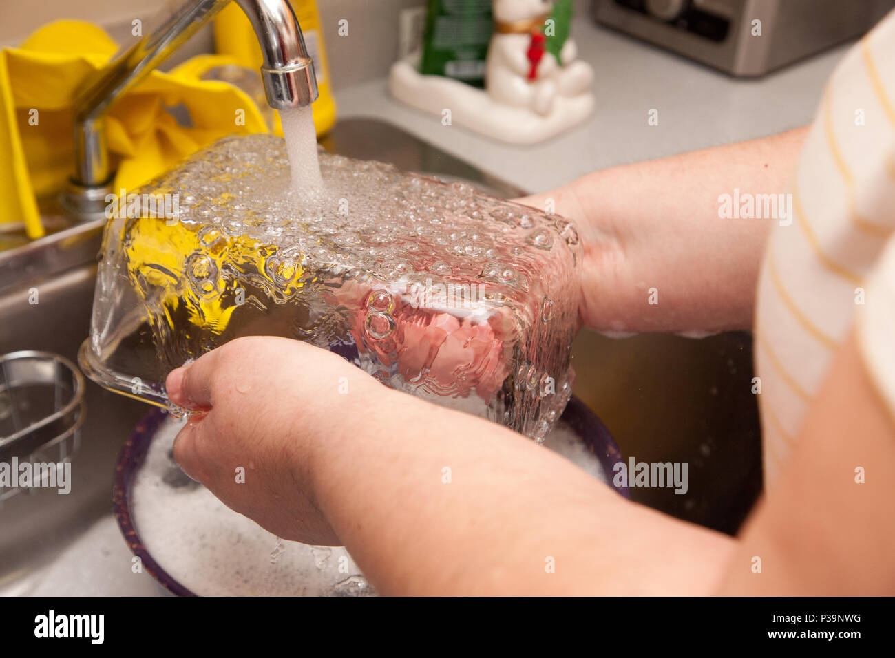 Wasser läuft über ein klares Glas Teller in die Spüle und gewaschen werden Stockfoto