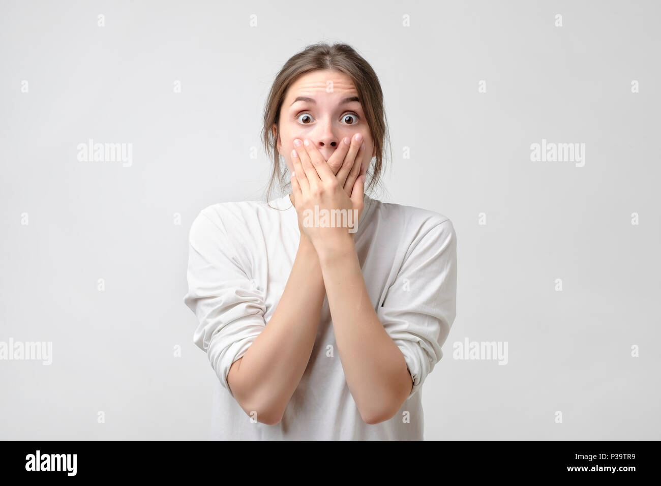 Attraktiv, hübsch und charmant, Frau geschlossen ihren Mund mit gekreuzten Händen und weit geöffneten Augen, in die Kamera zu schauen. Sie können nicht Ihre Augen glauben Stockfoto