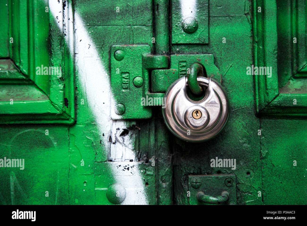 Eine Runde silber Vorhängeschloss ein Grün und Weiß graffiti Tür Stockfoto