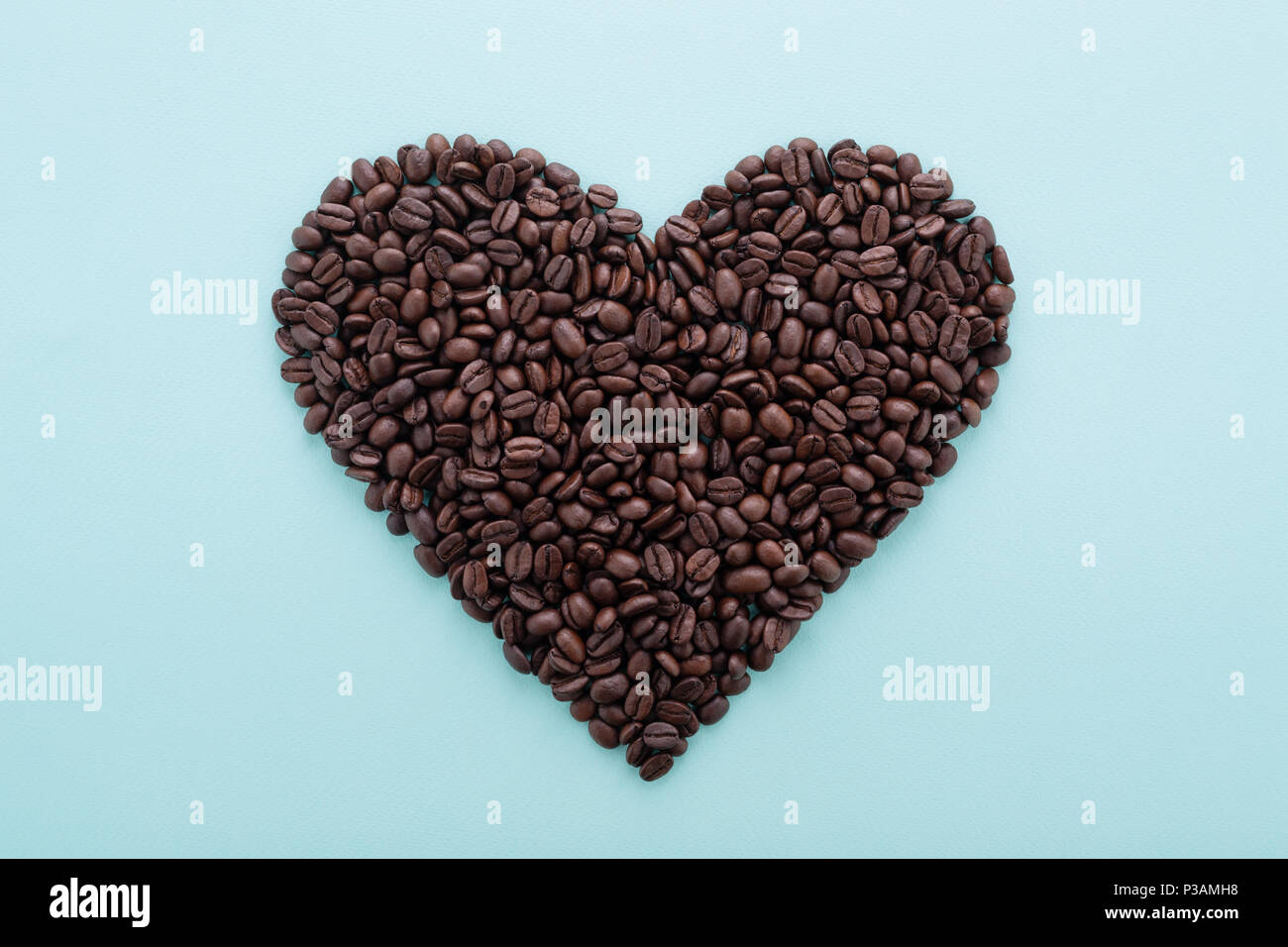 Perfekte Herzform aus Kaffeebohnen auf blauem Hintergrund. Flach, minimalistischen Design. Symbol der Liebe zum Kaffee. Stockfoto