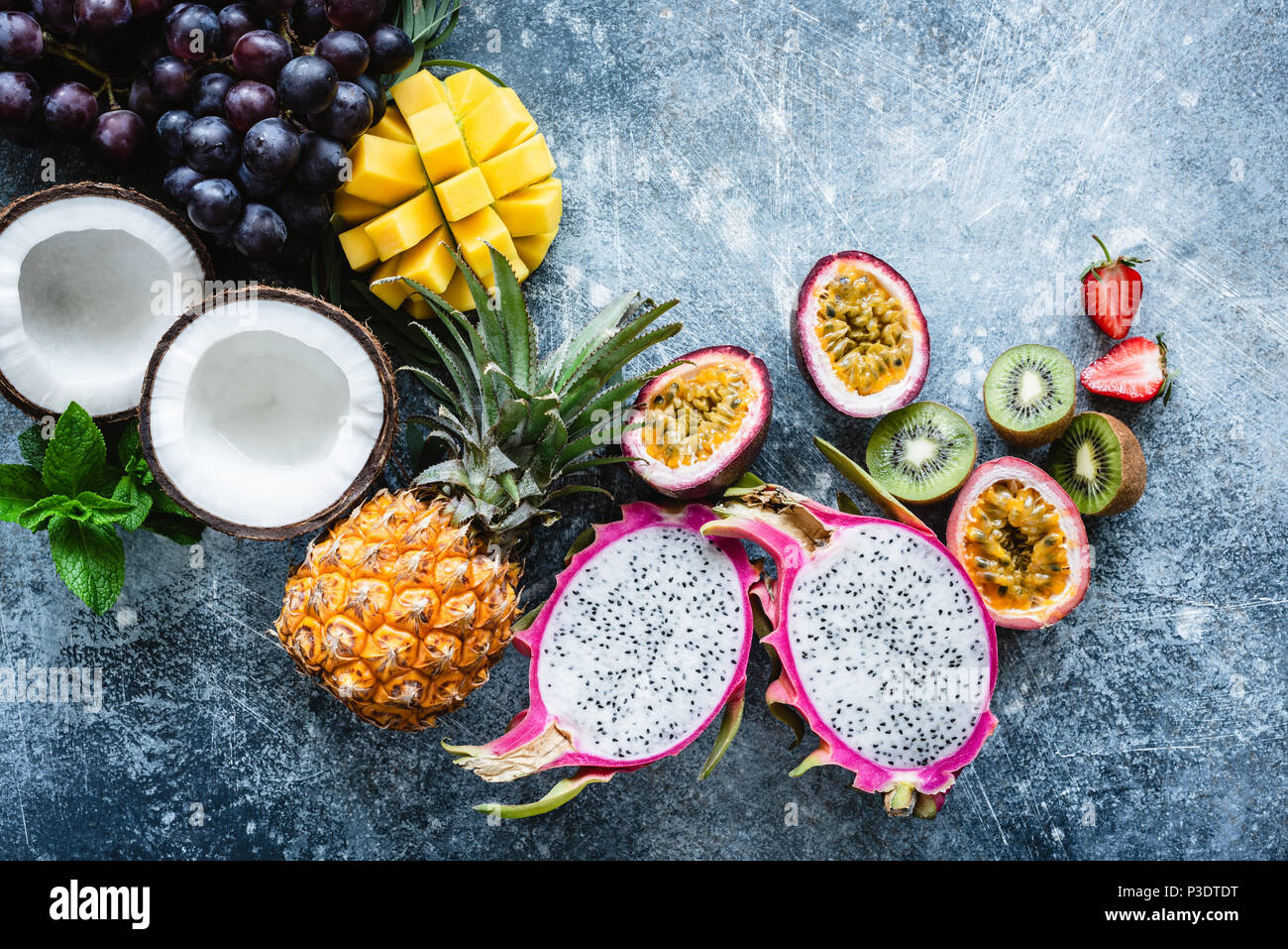 Gruppe von exotischen und tropischen Früchten. Mango, Drachenfrucht, Passionsfrucht, Kokos, Kiwi, Ananas und Erdbeere auf konkrete blauen Hintergrund. Frisches Obst Stockfoto