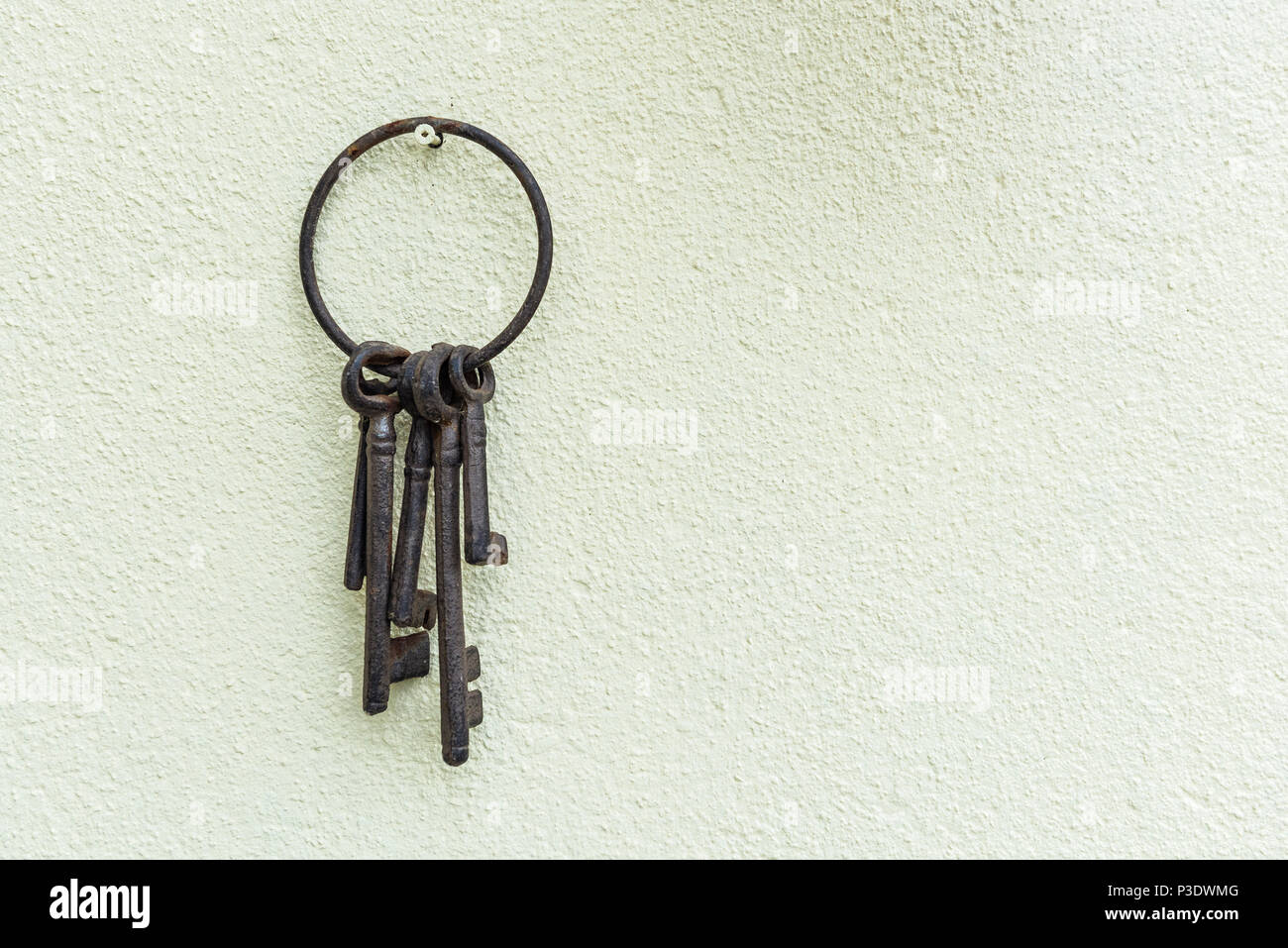 Rostige alte Schlüssel hängen an einer Creme texturierte Wand. Korrodierte Schlüsselanhänger aus Metall und Tasten. Stockfoto