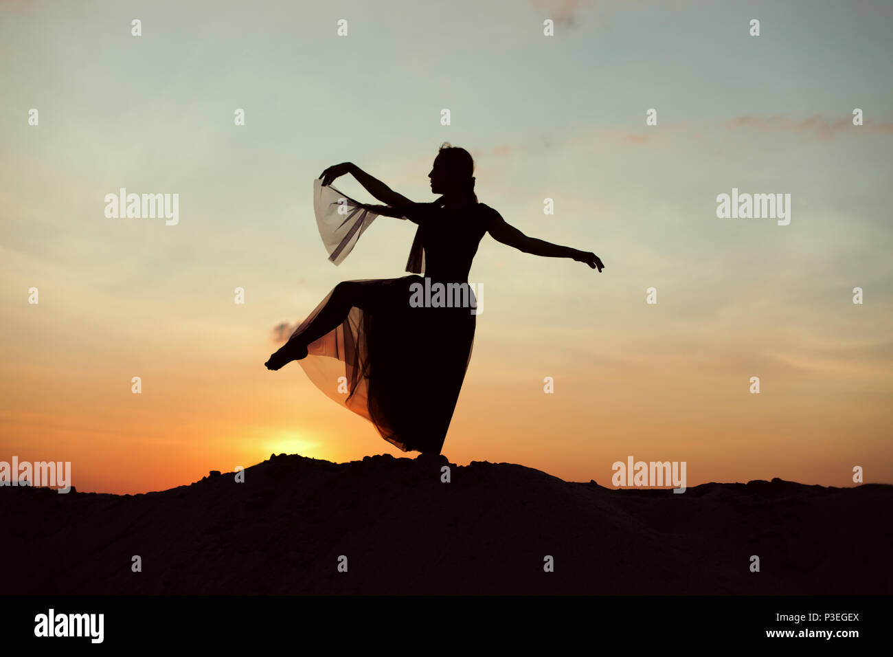 Silhouette einer Frau in der Wüste bei Sonnenuntergang, sie macht Tanzbewegungen. Stockfoto