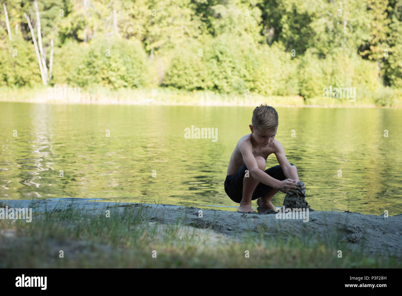 Junge spielt mit Sand in der Nähe der Flussufer Stockfoto