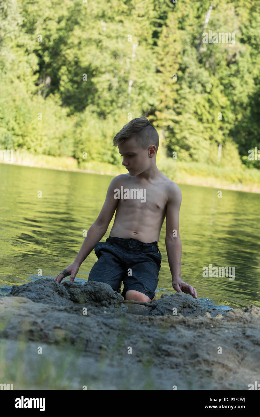 Junge spielt mit Sand in der Nähe der Flussufer Stockfoto