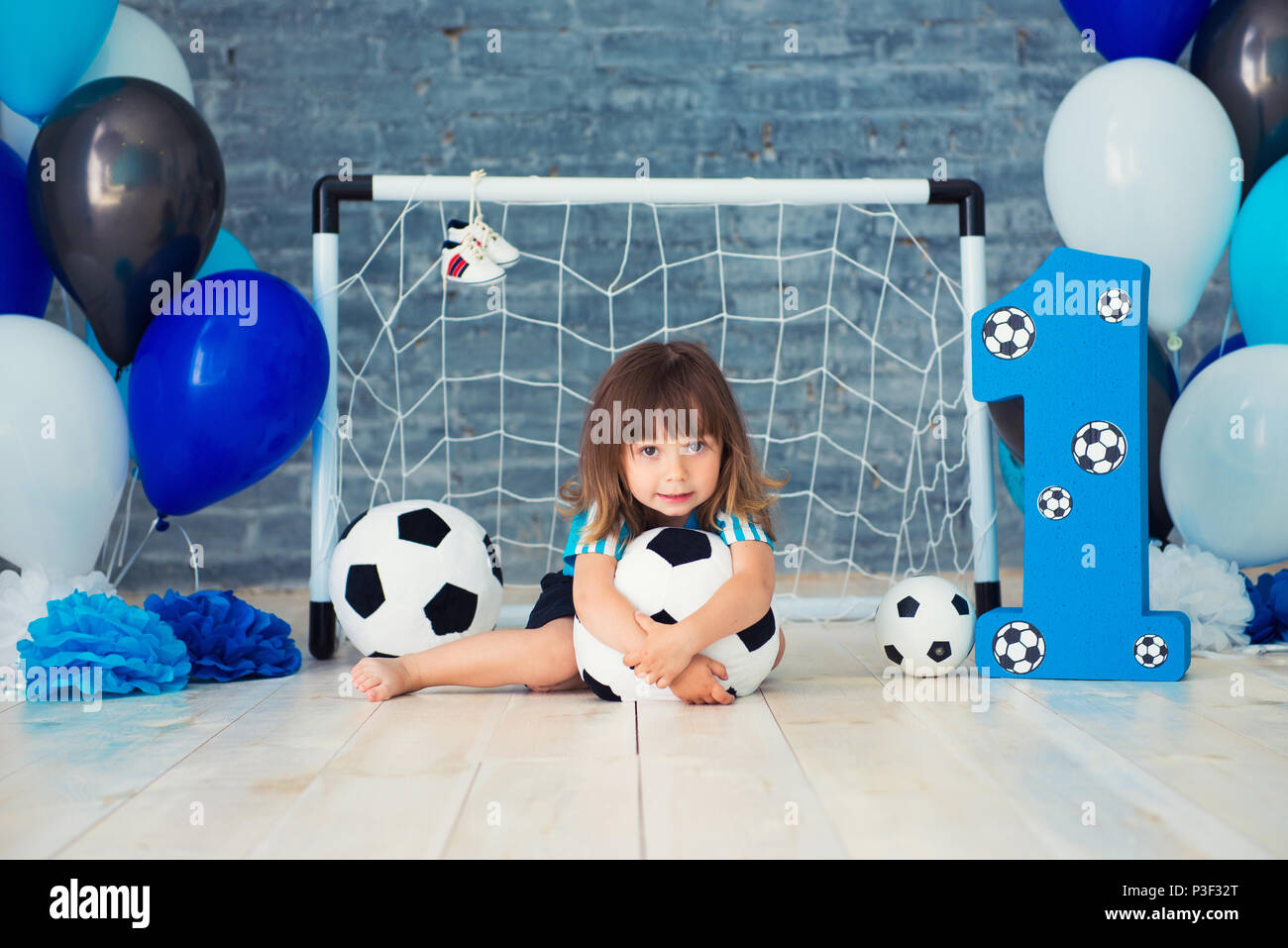 Wenig fröhliches Kind im Sport Kleidung sitzen auf dem Boden in der Nähe ein Fußballtor gekleidet, an einem großen Fußball schauen. Das erste Jahr, Nummer eins Stockfoto