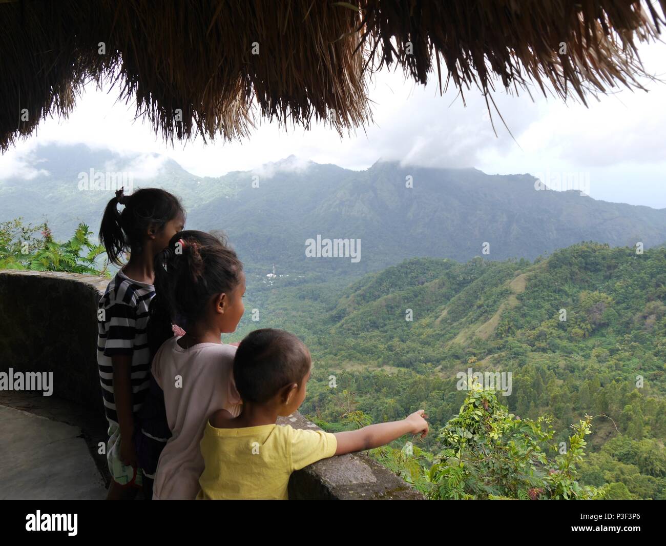 Drei junge indonesische Kinder genießen Sie einen Panoramablick auf die Berge auf der indonesischen Insel Flores und der kleine Junge Punkte an etwas Stockfoto