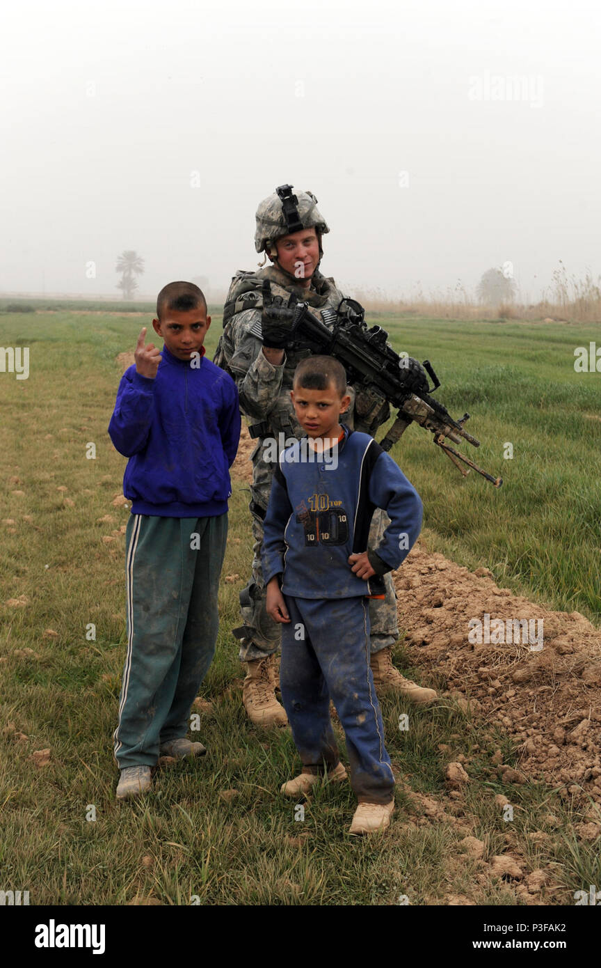 Ein US-Soldat mit 2Nd Platoon, Bravo Company, 1. Brigade, 37th Battalion, 1st Brigade Combat Team, 1. Panzerdivision, nimmt einen Bruch zu schlagen eine Pose mit ein paar Kindern während ein Indirektes Feuer Patrouille in der Nähe von Al-Mustafia, Irak, 24.02.23. Us-Soldaten führen IDFs Beweis der Mörtel launch Sites oder Angriffe gegen militärische instillations zu finden. Stockfoto