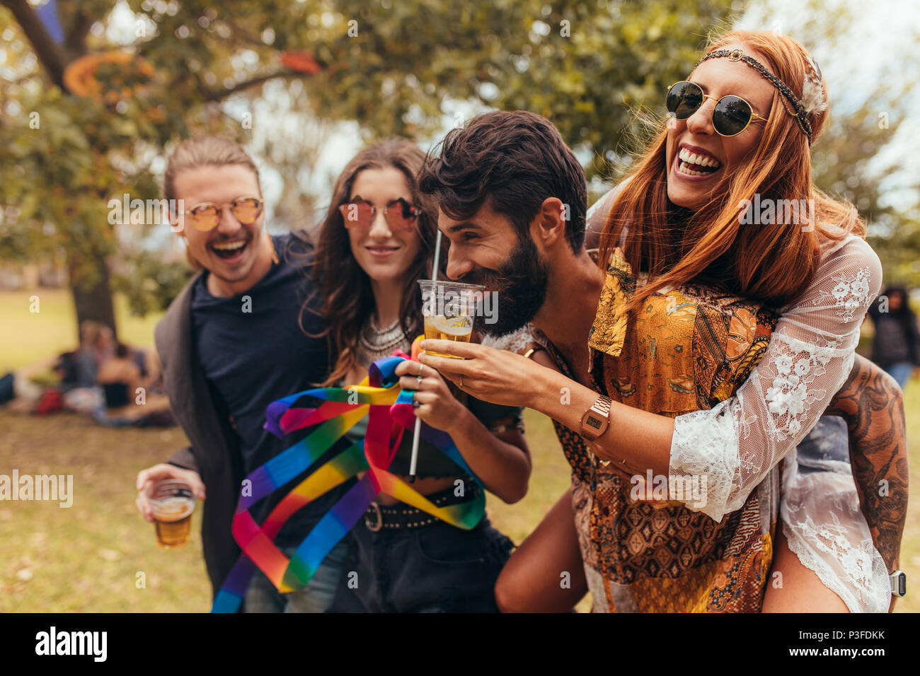 Junge Menschen im Summer Music Festival. Mann trinkt Bier von der Freundin Glas, während Ihr im Park huckepack. Stockfoto