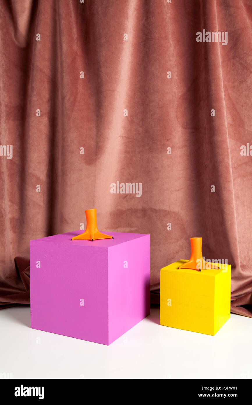2 orange Kunststoff ente Beine und farbige Würfel gelb und rosa. Minimal und geometrischen noch leben Farbe Fotografie Stockfoto
