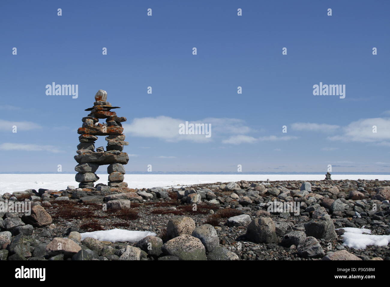 Inukshuk oder Inuksuk Wahrzeichen mit gefrorenen Bucht im Hintergrund in der Nähe von Arviat, Nunavut Stockfoto