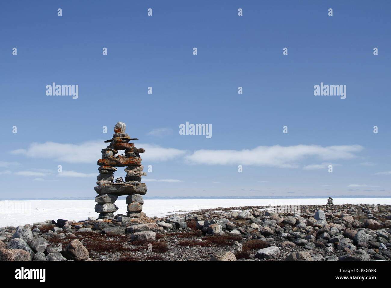 Inukshuk oder Inuksuk Wahrzeichen mit gefrorenen Bucht im Hintergrund in der Nähe von Arviat, Nunavut Stockfoto