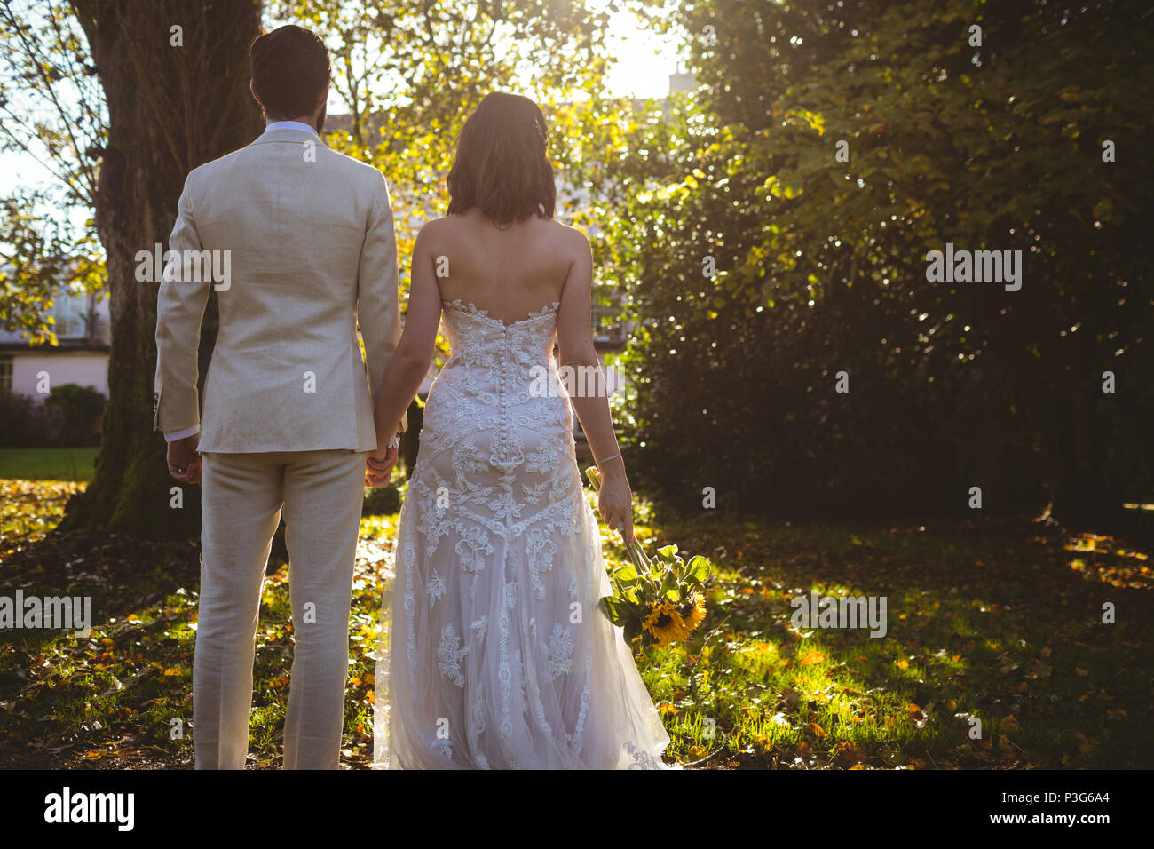 Braut und Bräutigam halten sich an den Händen und stehen im Garten Stockfoto