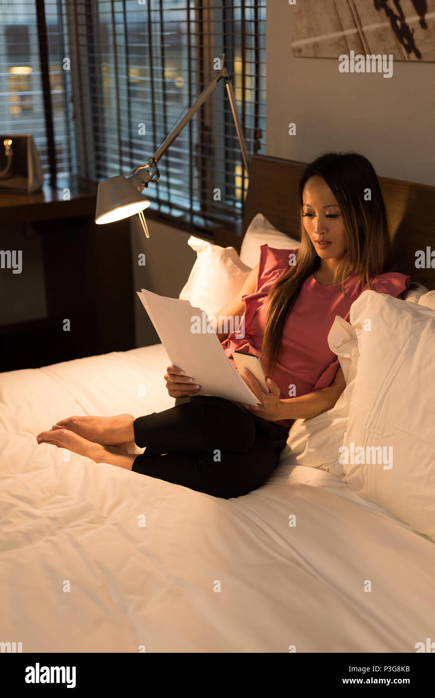 Geschäftsfrau, sitzen auf dem Bett Lesen von Dokumenten Stockfoto