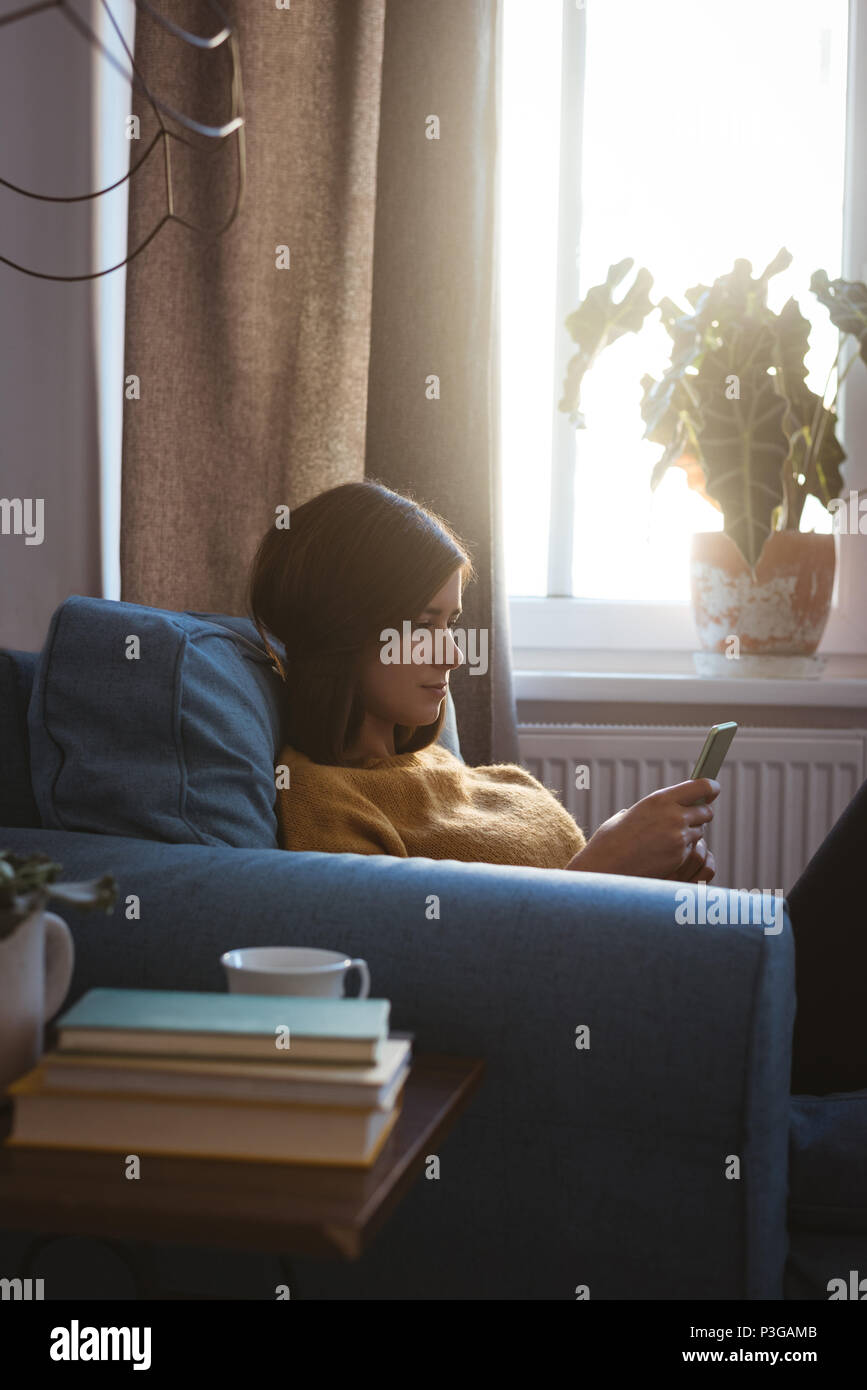 Junge Frau entspannt auf einem Sofa mit Ihrem Mobiltelefon im Wohnzimmer Stockfoto