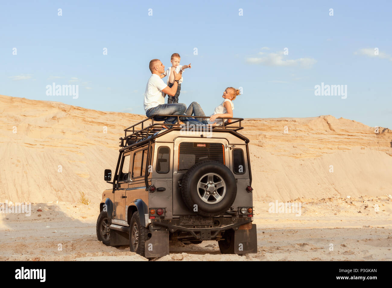 Portrait einer jungen Familie mit Sohn auf dem Dach des Autos in der Wüste. Stockfoto