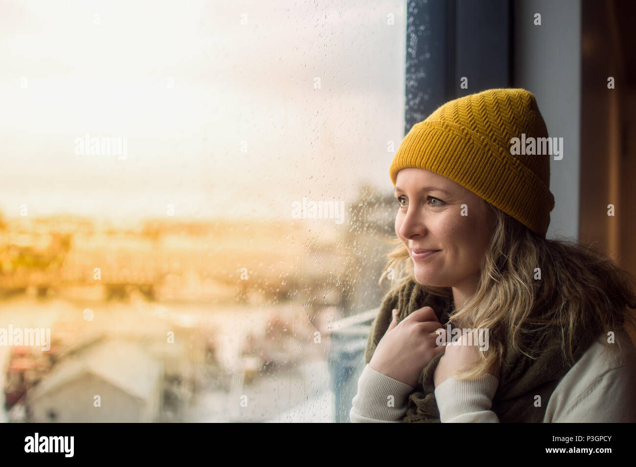 Frau tragen gelbe Mütze suchen außerhalb Fenster Stockfoto
