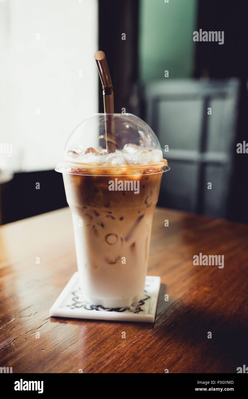 Iced Latte mit Stroh in Schale aus Kunststoff auf Holz Tisch im Café, Café Freizeitaktivitäten lifestyle Stockfoto