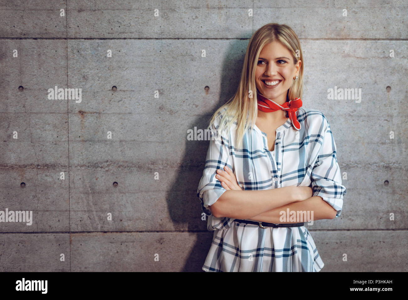 Junge schöne Erfolgreiche lächelnd weibliche Unternehmer stehen vor einer Betonwand mit gekreuzten Händen und Kamera. Stockfoto