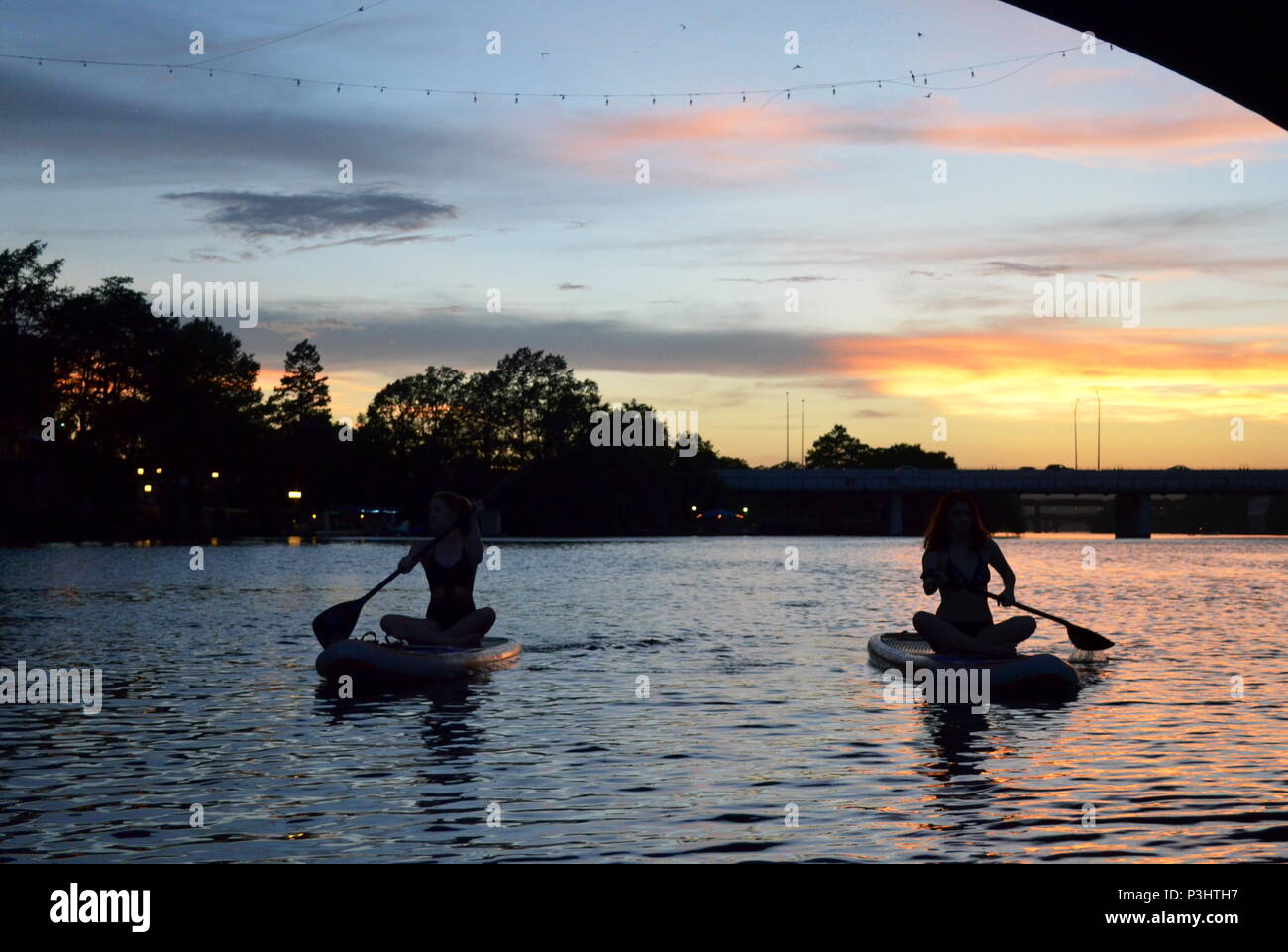 Zwei Mädchen Paddle Boarding am Abend die der Kongress Ave Fledermäuse zu beobachten ein Marienkäfer See in Austin, Texas. Stockfoto