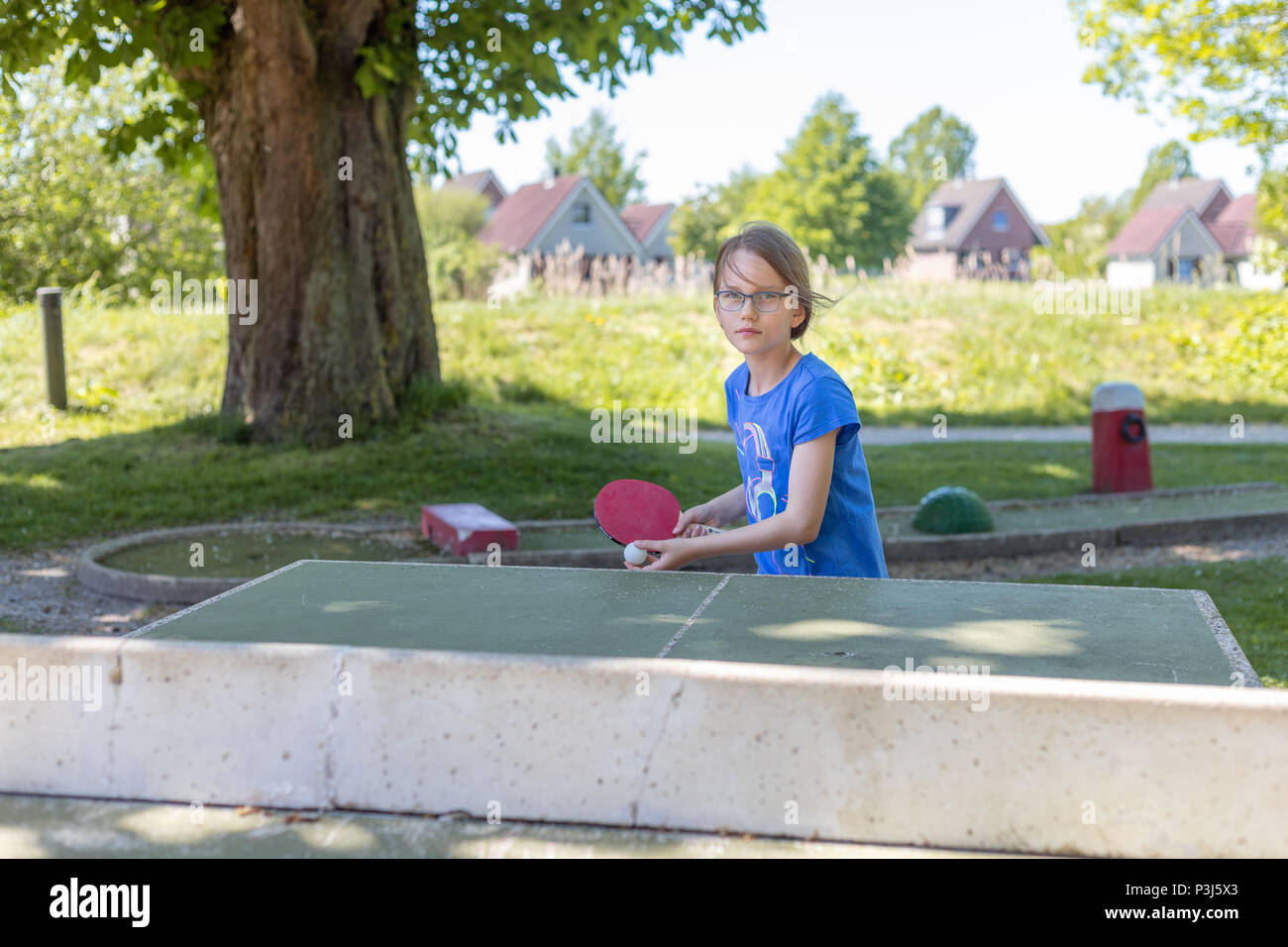 Ein 9 Jahre altes Mädchen spielt Tischtennis auf eine Tischtennisplatte. Sie spielt das erste Service Stockfoto
