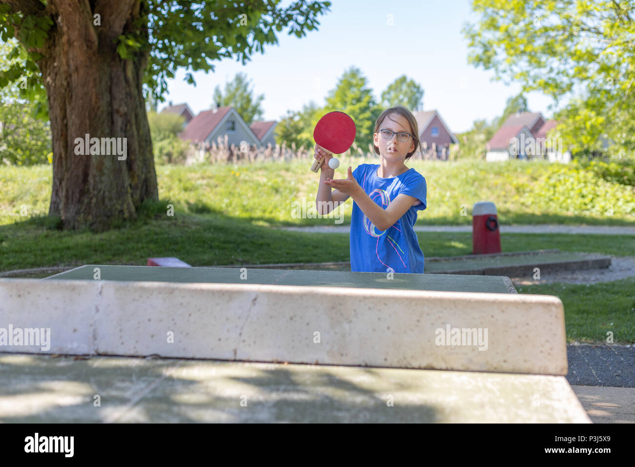 Ein 9 Jahre altes Mädchen spielt Tischtennis auf eine Tischtennisplatte. Sie spielt den ersten Aufschlag Stockfoto
