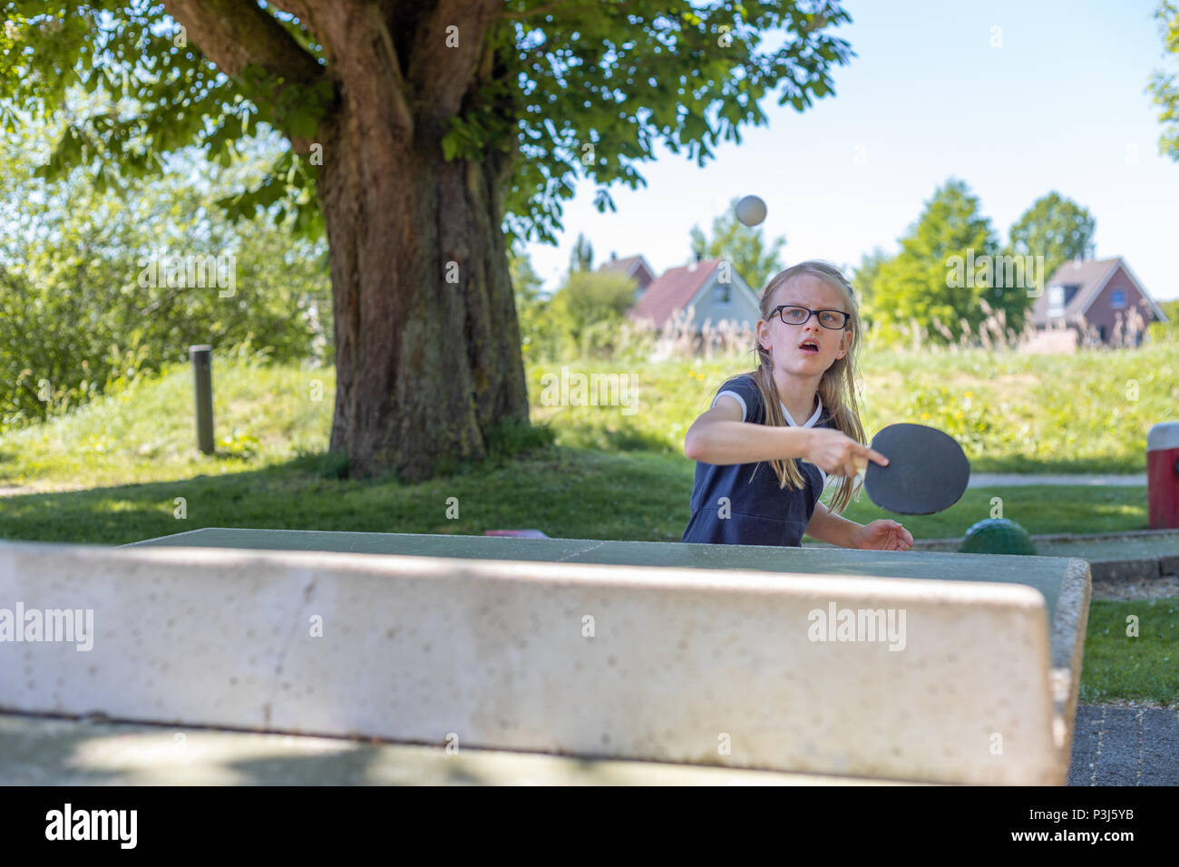 Ein 7 Jahre altes Mädchen spielt Tischtennis auf eine Tischtennisplatte. Sie ist auf dem Schlagen Sie den Ball mit Ihrem Schläger konzentriert Stockfoto