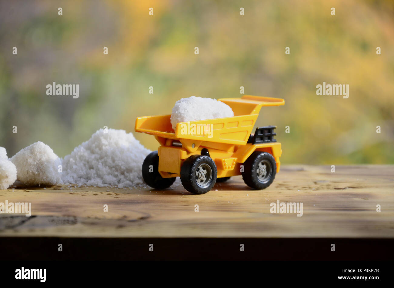 Ein kleines gelbes Spielzeug-LKW ist mit einem Stein der Weißen Salz neben einem Haufen Salz geladen. Ein Auto auf einer holzfläche vor dem Hintergrund der Herbst Wald. Stockfoto