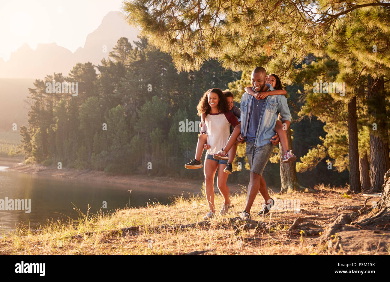 Eltern geben Kindern Piggyback Rides auf Spaziergang am See Stockfoto