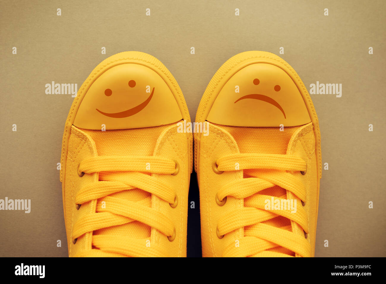 Glückliche und traurige Smiley Emoticon Symbol auf gelbem Sneakers, konzeptionelle Bild für Gefühle und Emotionen der jungen Menschen und Jugendlichen Stimmungsschwankungen Stockfoto