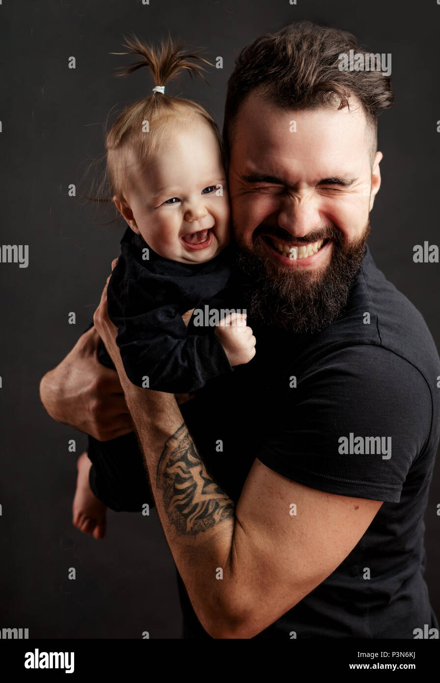 Stattliche tätowierten jungen Mann mit niedlichen kleinen Baby auf schwarzem Hintergrund Stockfoto