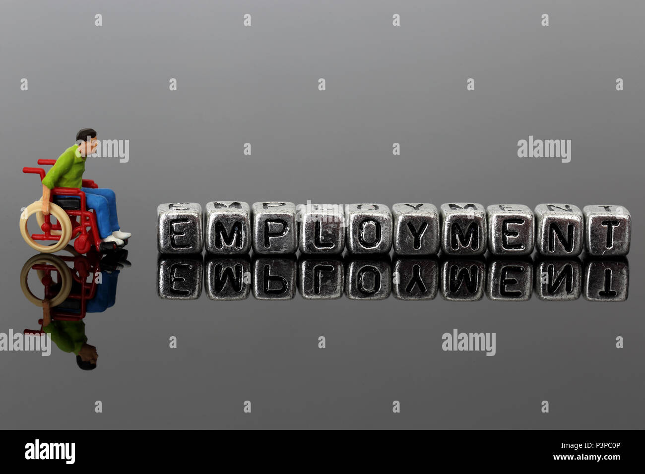 Miniatur Modell Mann im Rollstuhl mit dem Wort Beschäftigung auf Perlen auf einem dunklen Hintergrund reflektiert Stockfoto