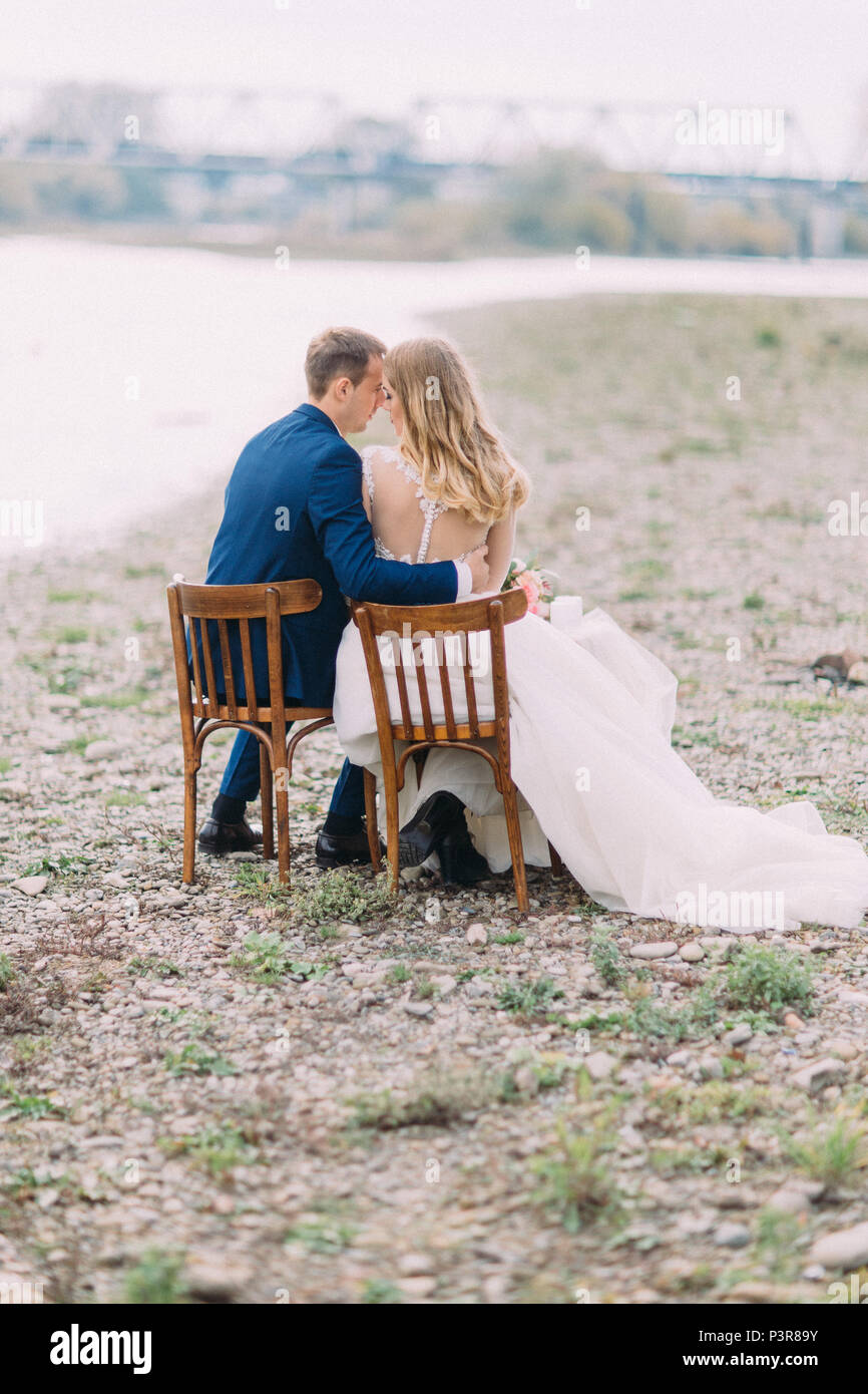 Die volle Länge zurück Blick auf dem Brautpaar während der Sitzung auf den Stühlen an der Küste. Stockfoto