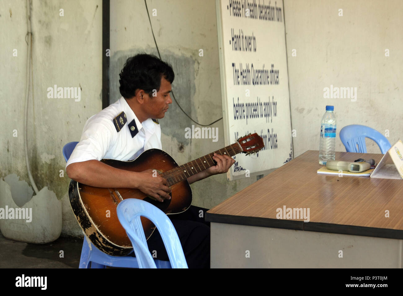 Cham Yeam; am Grenzübergang Check Point zwischen Kambodscha und Thailand eine entspannte Quarantäne Offizier spielt eine abgenutzte Gitarre. Stockfoto