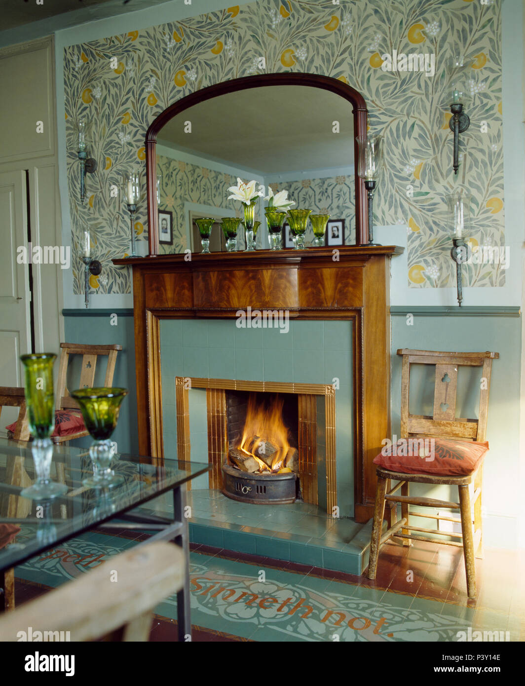 Stenciled Kunst + Handwerk Muster an der Wand über dem Kamin mit brennenden Feuer im Land Esszimmer Stockfoto