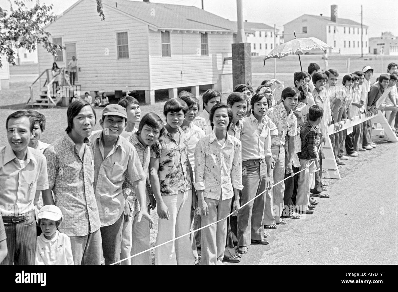 FORT SMITH, AR, USA - 10. AUGUST 1975 - eine Linie der neu angekommenen Vietnamesische Flüchtlinge stehen und für die Weitergabe von Präsident Gerald Ford warten. Der Präsident ist zu touring das Fort Chaffee vietnamesischer Flüchtling Zentrum sein und einladend Die evakuierten Südvietnamesischen in die Vereinigten Staaten. Hinter den Menschen steht die Zeilen der Kasernengebäude, dass die Flüchtlinge untergebracht. Stockfoto