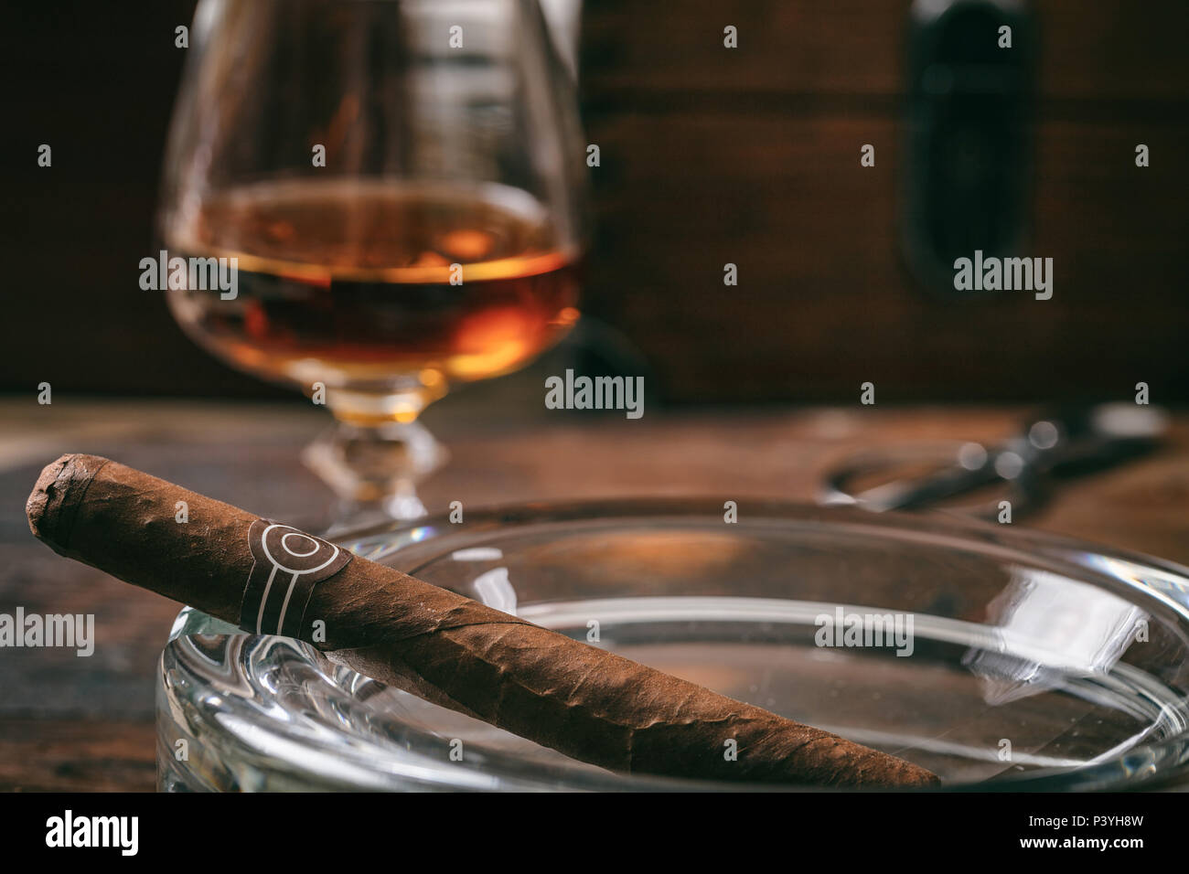 Kubanische Zigarre in einem Aschenbecher, ein Glas Brandy, Holz- Hintergrund, Kopieren, coseup Ansicht mit Details Stockfoto