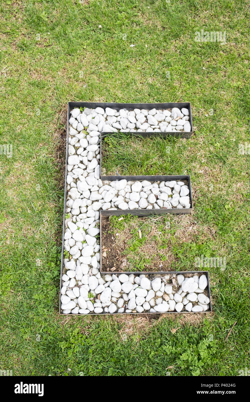 Buchstaben E, gebaut aus weißen Steinen auf grünem Gras als von oben gesehen Stockfoto
