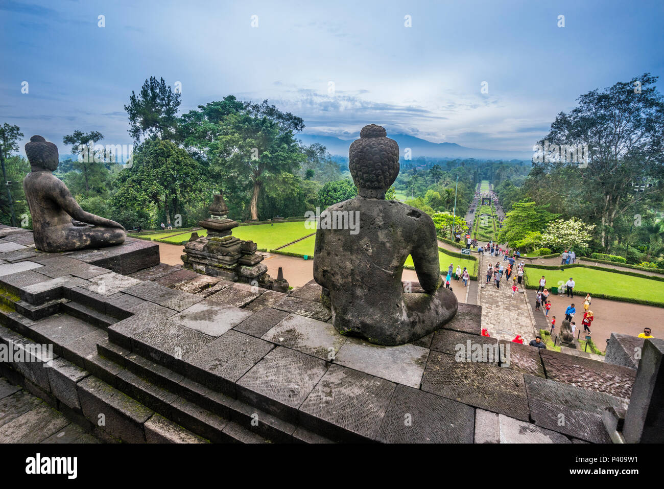 Eine heitere sitzender Buddha Uhren auf als Besucher Menschenmassen mak ihren Weg zu den Aufstieg des 9. Jahrhunderts Borobudur buddhistischen Tempel, Zentraljava, Indonesien Stockfoto